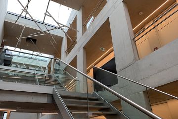 Lichtdurchflutetes Treppenhaus in moderner Betonoptik mit gläsernen Treppengeländern