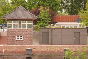 Ein kleines Gebäude mit einer Fassade aus graubraunen Platten direkt am Wasser