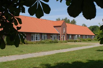 Das lange Gebäude des Seniorenzentrum Nord e.V. mit roten Ziegeln, roten Dachpfannen und einem hervorgehobenem Giebel im Eingangsbereich