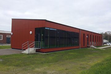 Ein kleines Gebäude mit gläsernem Eingang und mit rostroten Platten verkleideter Fassade