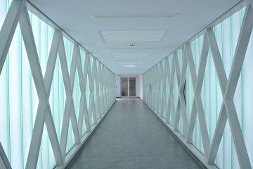 Ein langer Verbidungsgang mit bodenlangen, lichtdurchlässigen Milchglasscheiben links und rechts